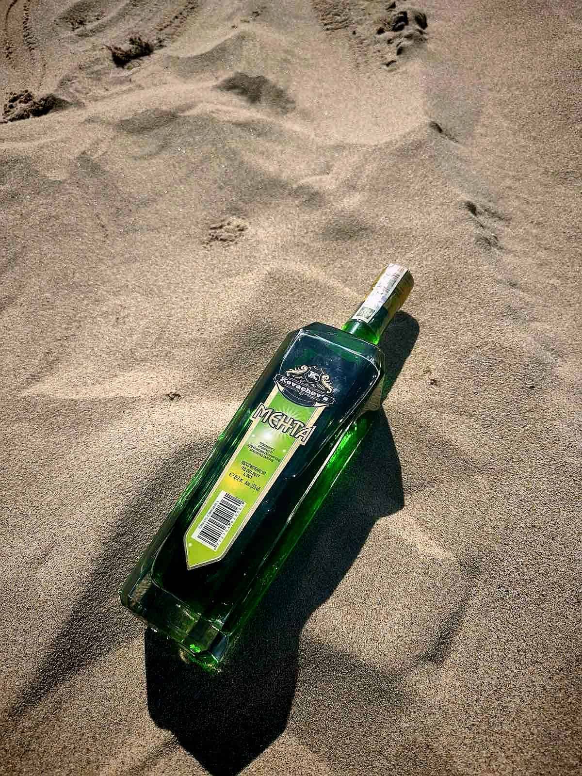 Green bottle of Russian vodka partially buried in sandy beach sand.